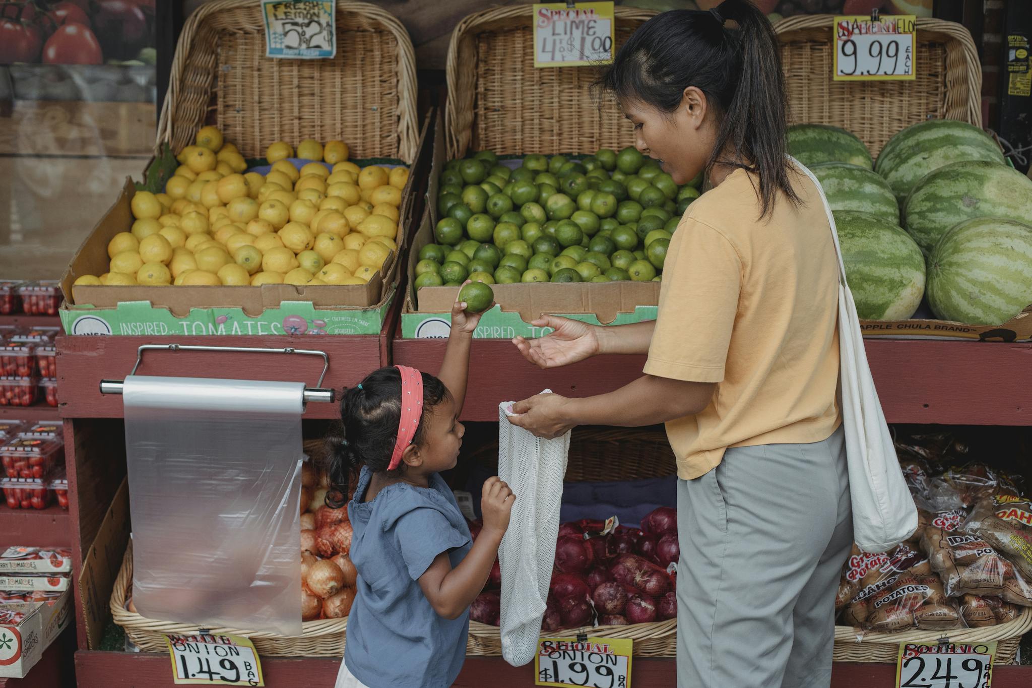 Back view Asian woman with daughter wearing casual outfits standing near local street market stall and choosing fruits