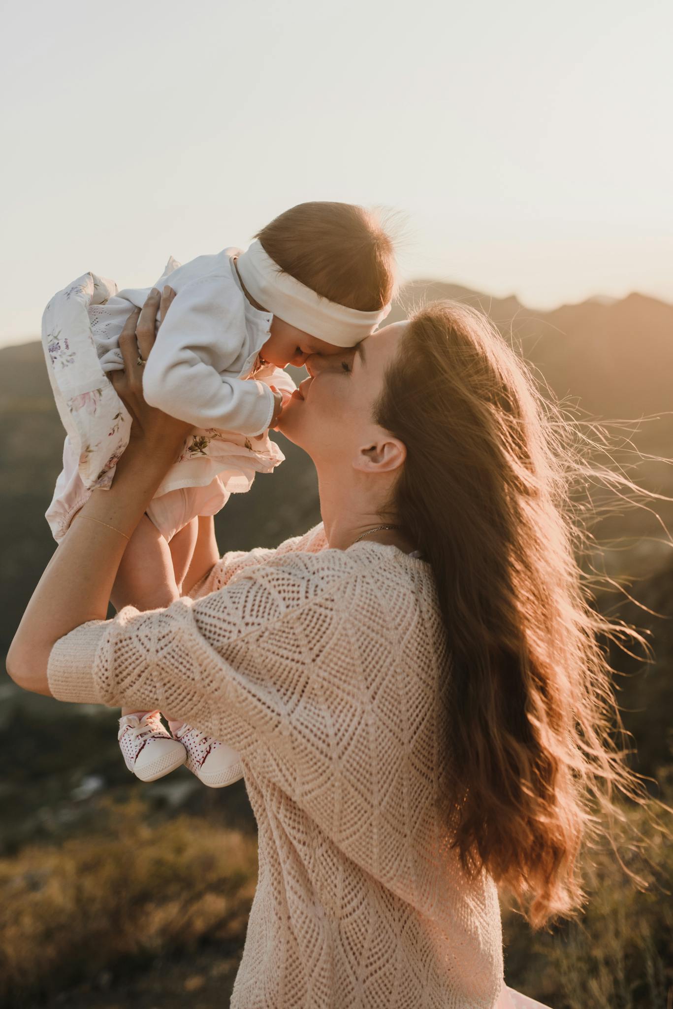 Heartwarming scene of a mother lifting her baby with tender joy during sunset.