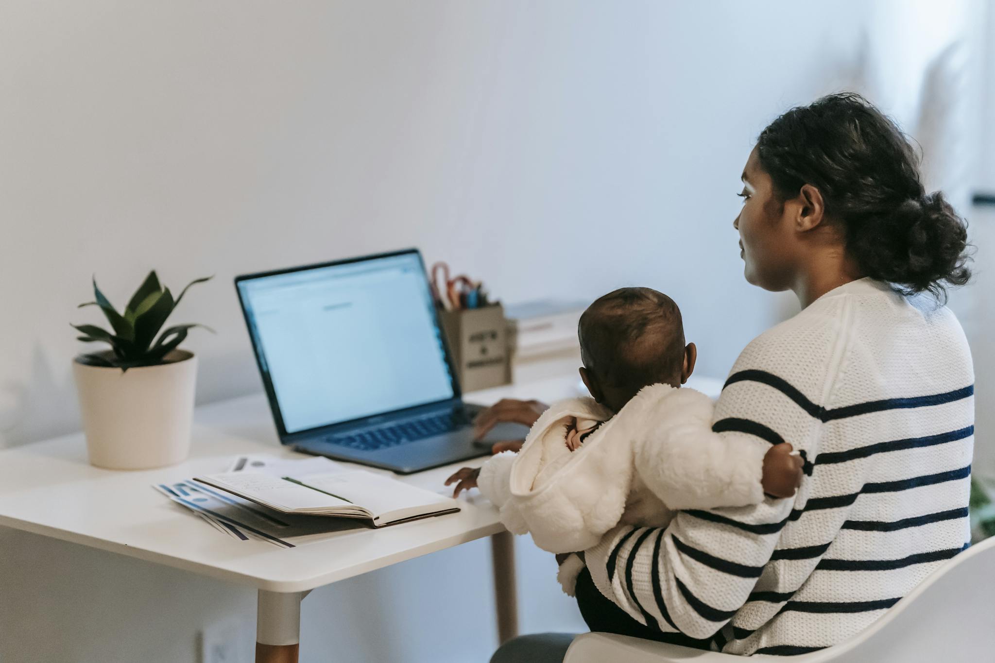 Pensive ethnic woman in casual clothes slitting with baby while browsing netbook in light room in apartment in daytime